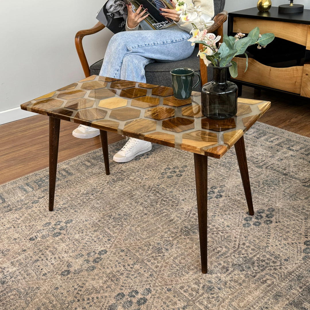 A woman sitting on a couch beside a walnut epoxy coffee table with a honeycomb pattern.