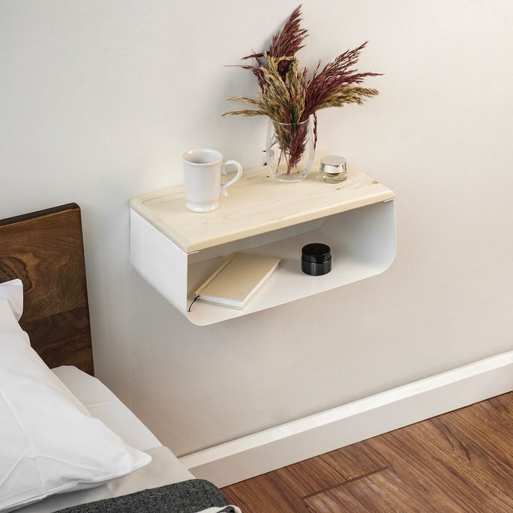 A floating nightstand with a wooden top, featuring a cup and a book on its shelf.