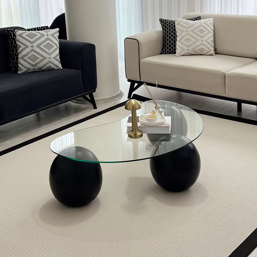 Contemporary glass coffee table on two black ball legs on a cream rug between two sofas