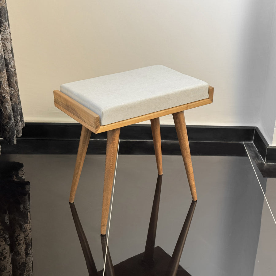 Walnut piano bench with a cream upholstered cushion and four tapered legs, in a room corner
