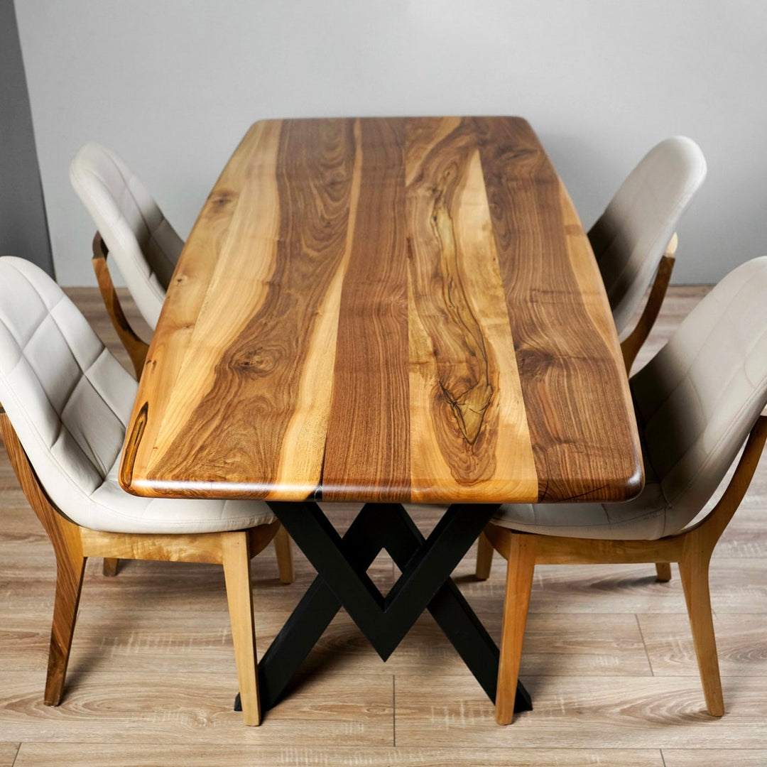 Top view of a walnut dining table on a black X-shaped steel base, its boards showing dark brown heartwood streaked with pale cream sapwood, with four light upholstered chairs around it