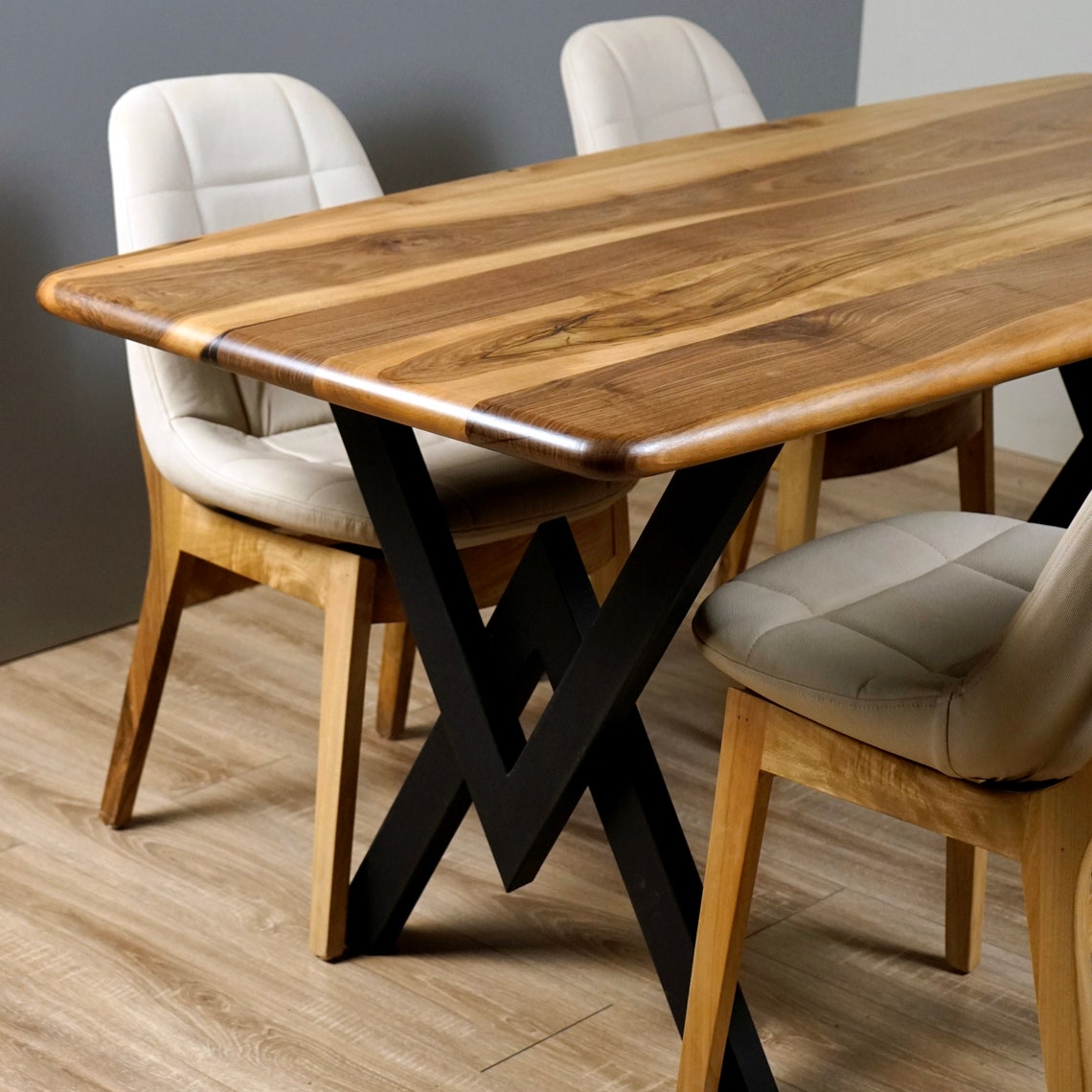 Solid walnut dining table with smooth rounded edges on a black steel X base, with light upholstered dining chairs