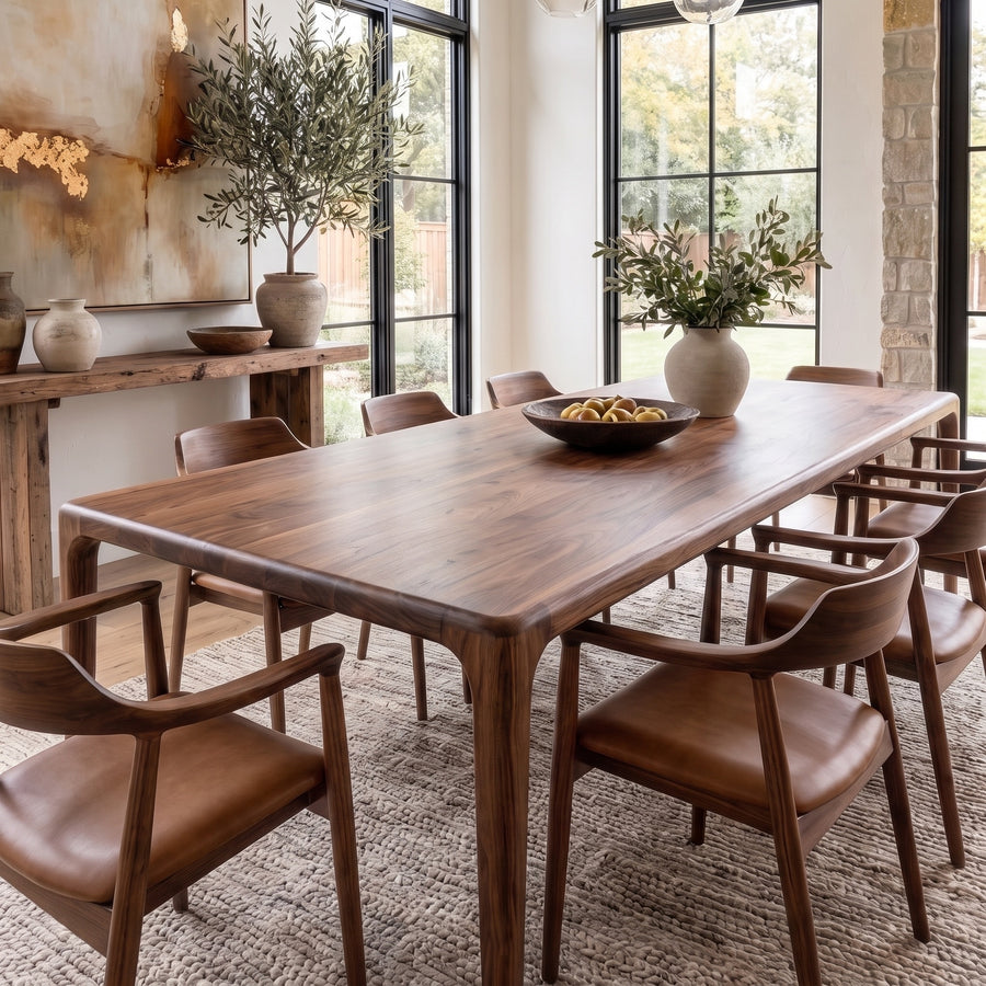 Oslo solid walnut dining table with rounded edges and tapered legs, set with brown leather armchairs in a bright dining room