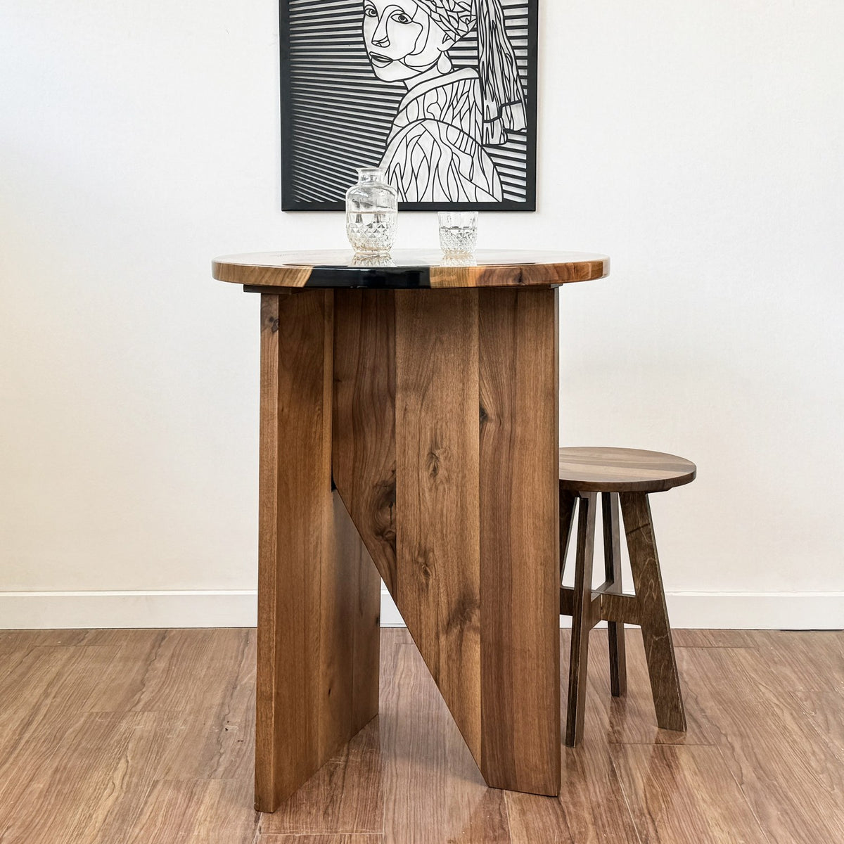 Side view of the walnut bar height table's slab base and black epoxy river top with a stool