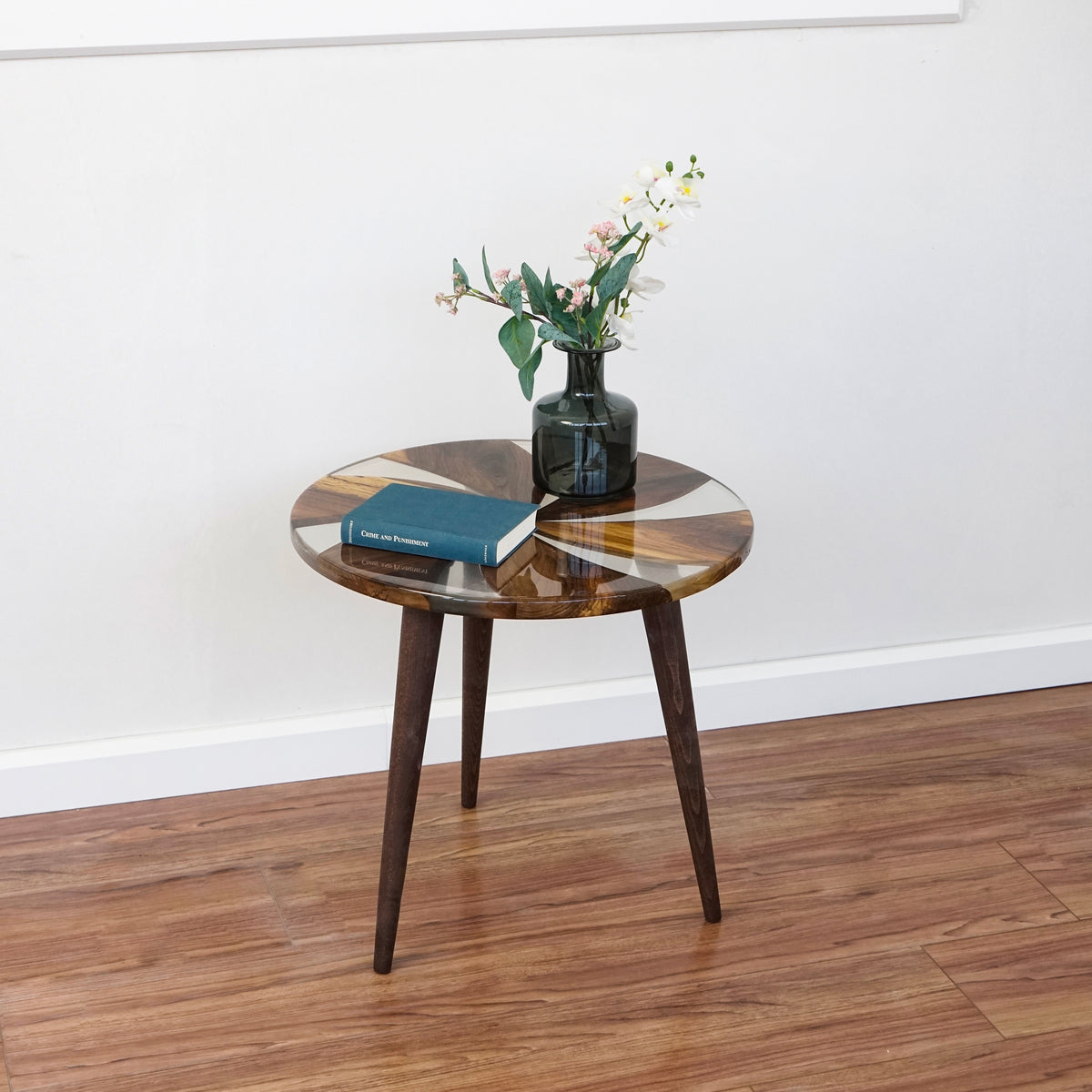 Round walnut side table with clear epoxy windmill pattern and three tapered dark legs, front view