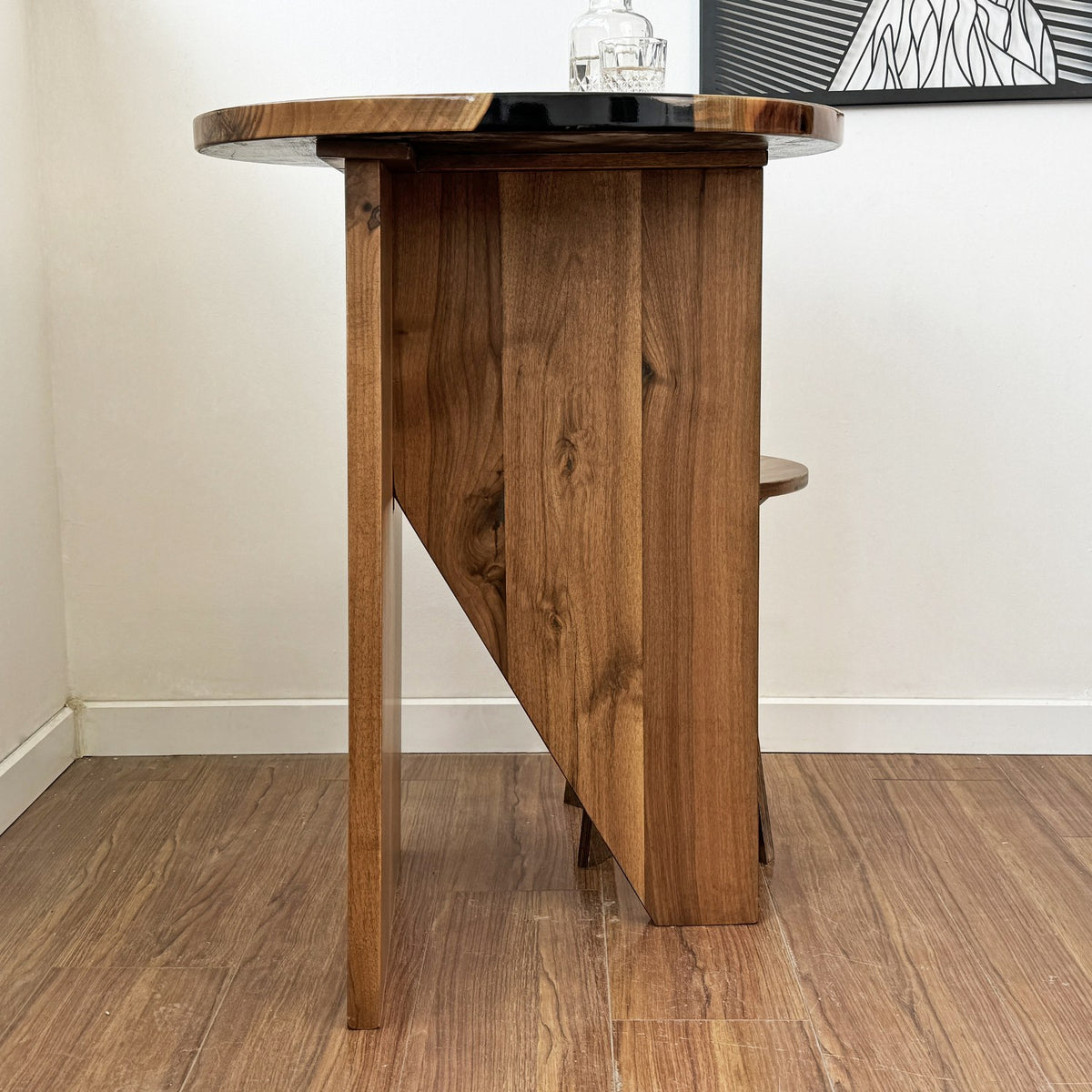 Tall walnut bar table seen from the side with its angled slab base, the top cropped at the edge