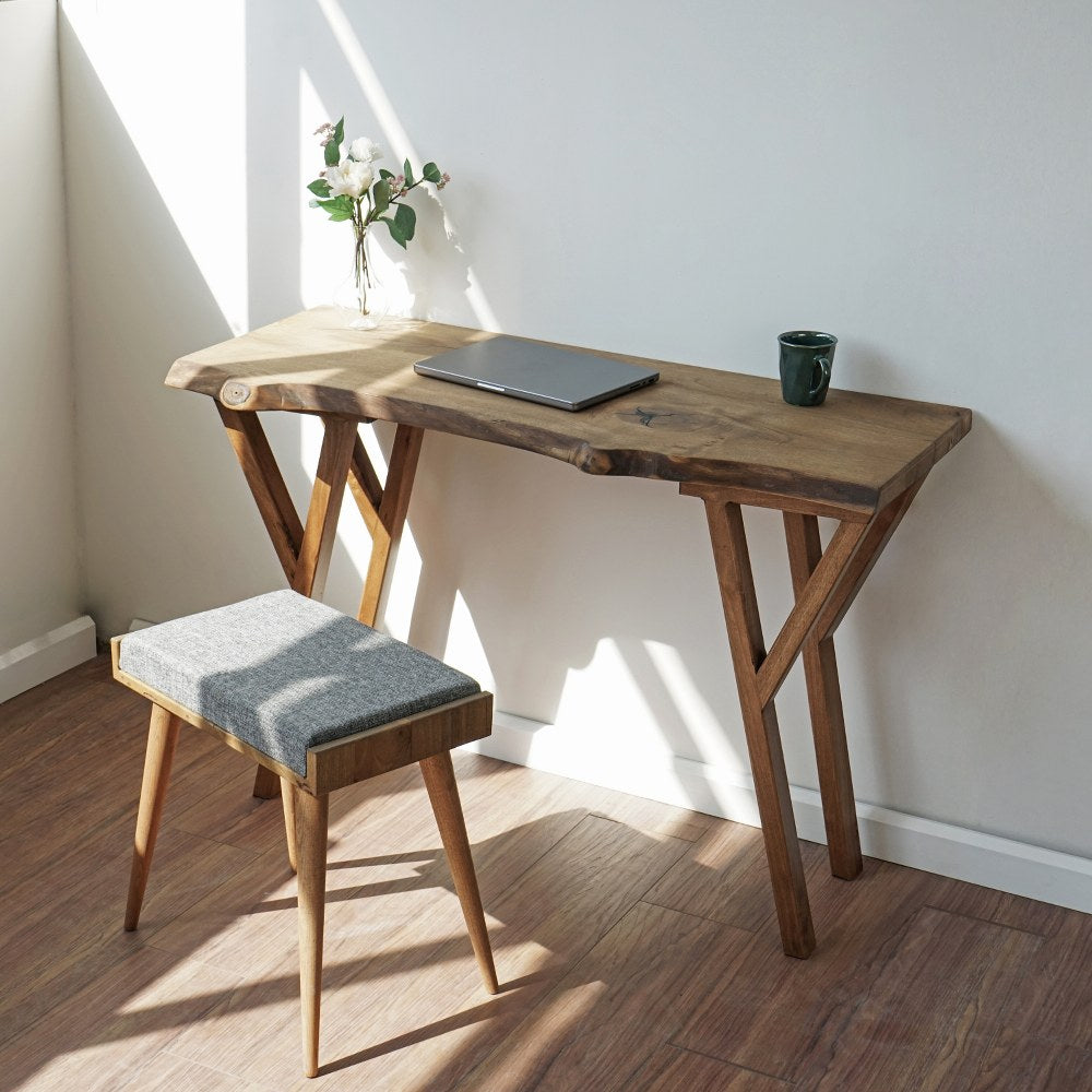 Three-quarter view of the small live edge walnut desk with Y-legs and a gray stool underneath