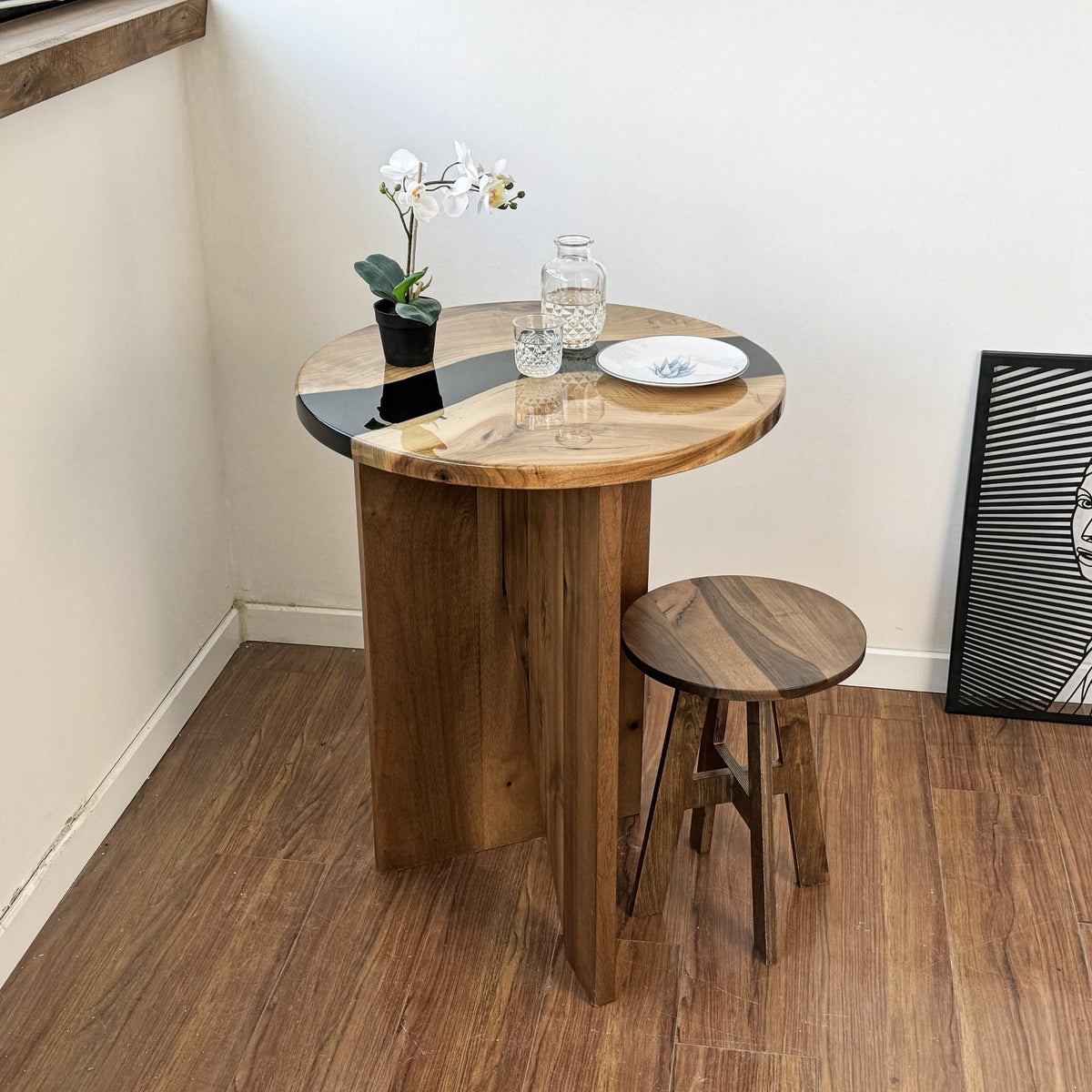 Walnut round bar table with a plate and an orchid on the epoxy river top, corner room view