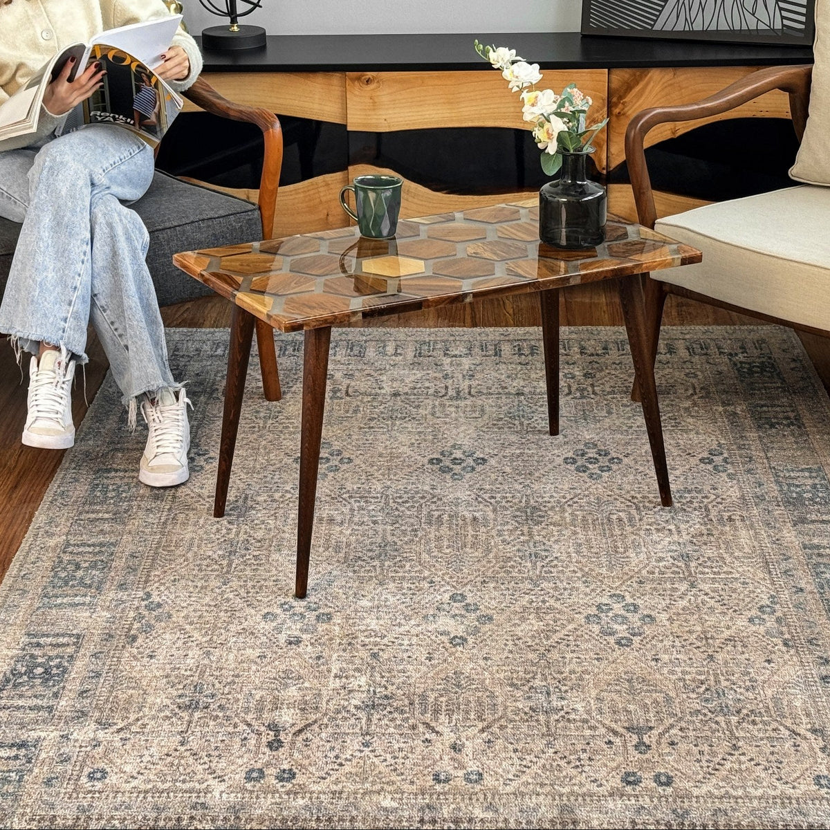 Distant view of the honeycomb walnut epoxy coffee table on a patterned rug in front of a sideboard
