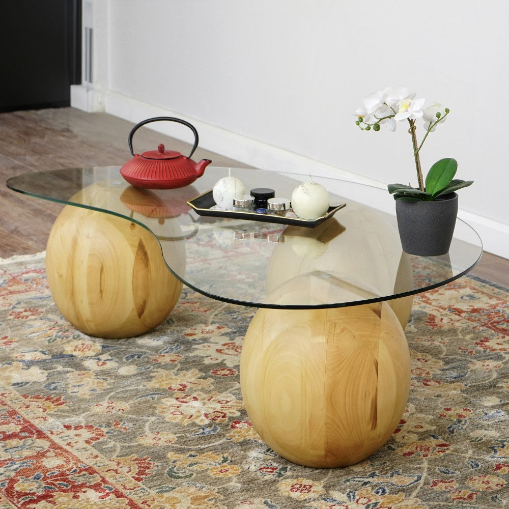 Glass top coffee table with spruce ball legs, wide three-quarter view on a patterned rug