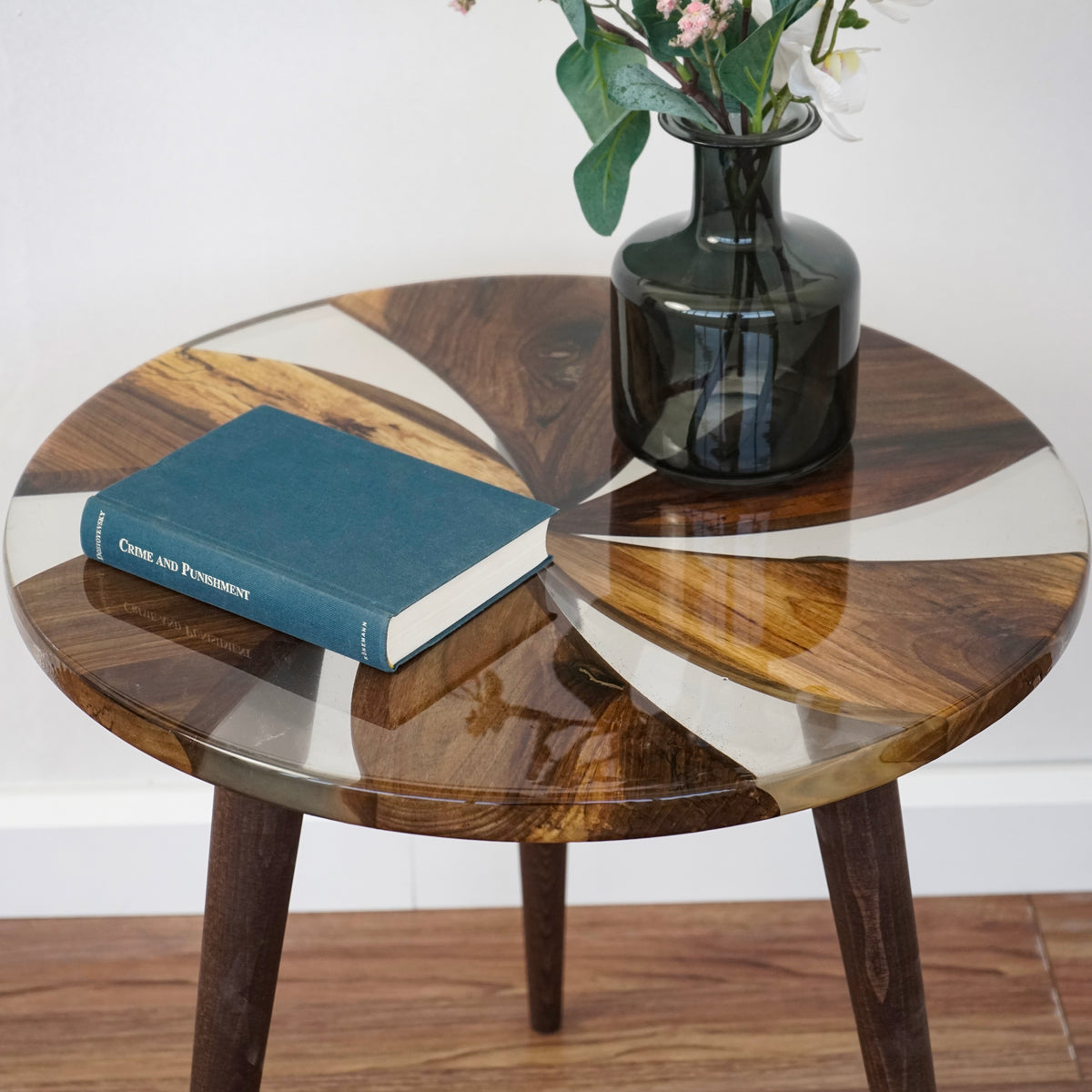Tabletop close-up of the walnut and clear epoxy windmill side table with a book and dark glass vase