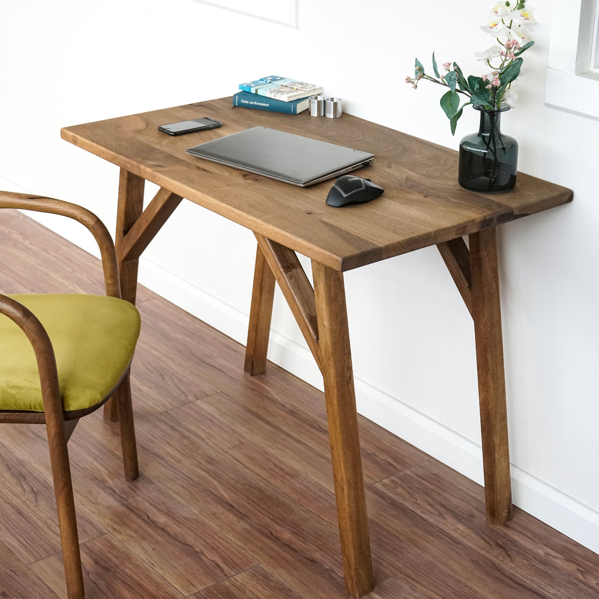 Small walnut desk with rectangle front edge and splayed legs beside a green armchair, angled view