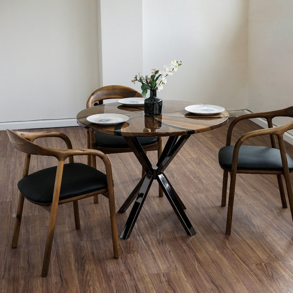 Round walnut dining table with black epoxy swirl on glossy dark crossed metal legs, three armchairs around it