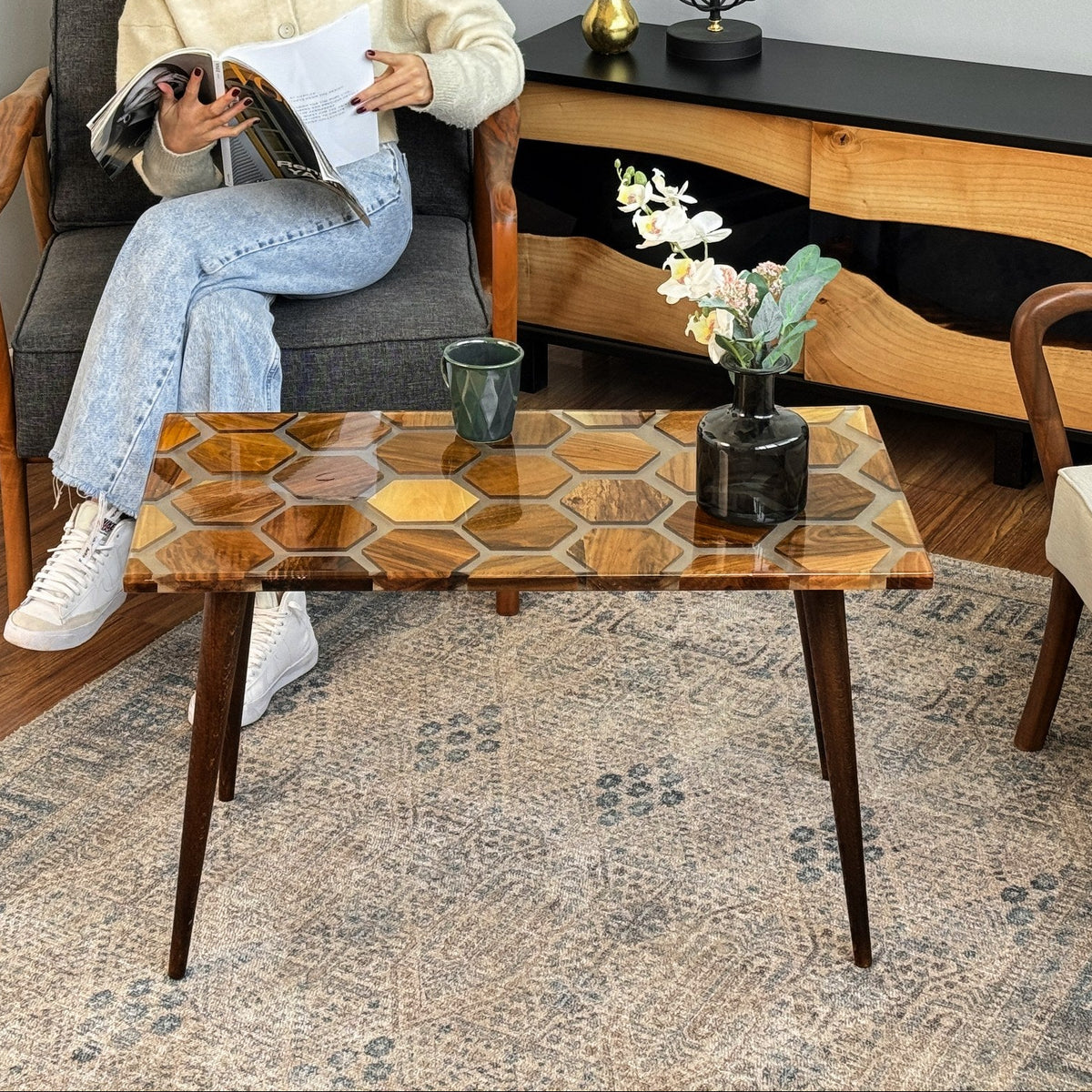 Front view of the honeycomb walnut epoxy coffee table in a living room with a seated reader