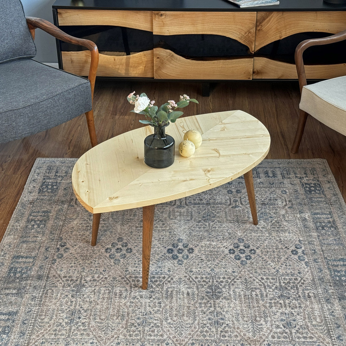 Leaf shaped coffee table with a pale natural wood top and dark tapered legs on a rug