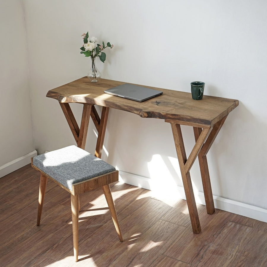 Small live edge walnut desk with a laptop and a gray upholstered stool in a corner