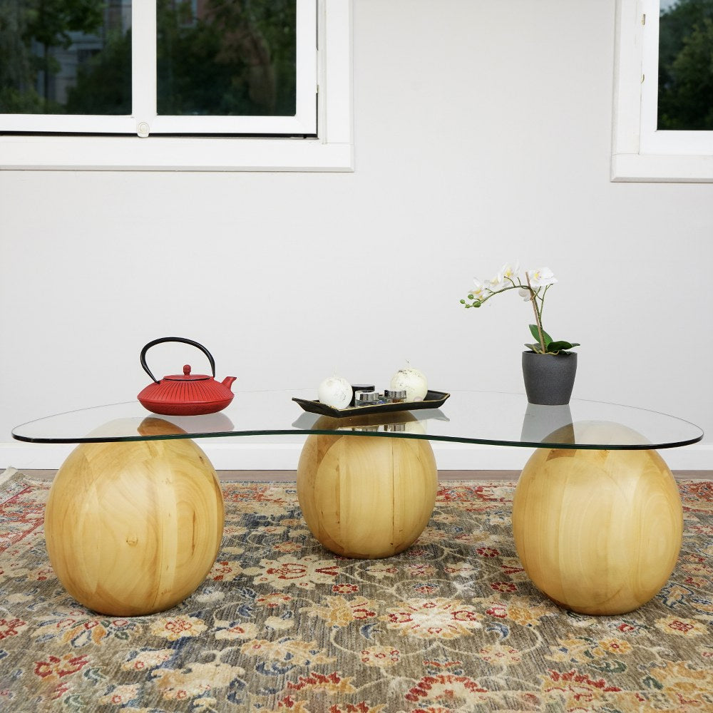 Front view of the bean shaped glass coffee table with three wooden ball legs on a rug