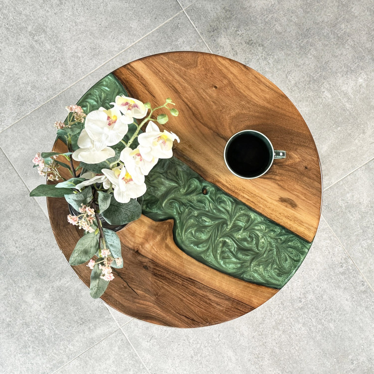 Top-down view of the round walnut epoxy side table with the green resin river and a mug
