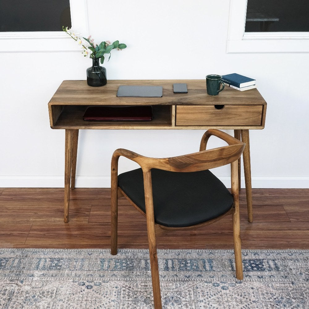 Front view of the walnut boho desk with open cubby and drawer, armchair pulled out on a rug