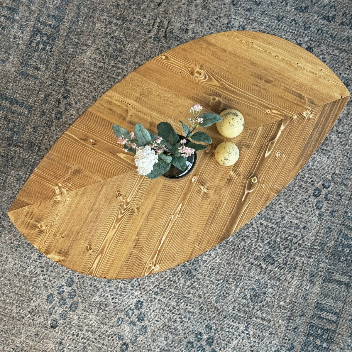 Angled top view of the leaf shaped coffee table showing the chevron plank pattern on a rug