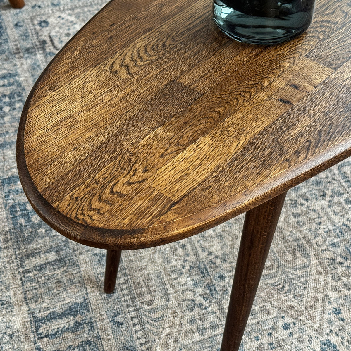 Close-up of the rounded edge, oak plank grain and tapered leg of the oval coffee table