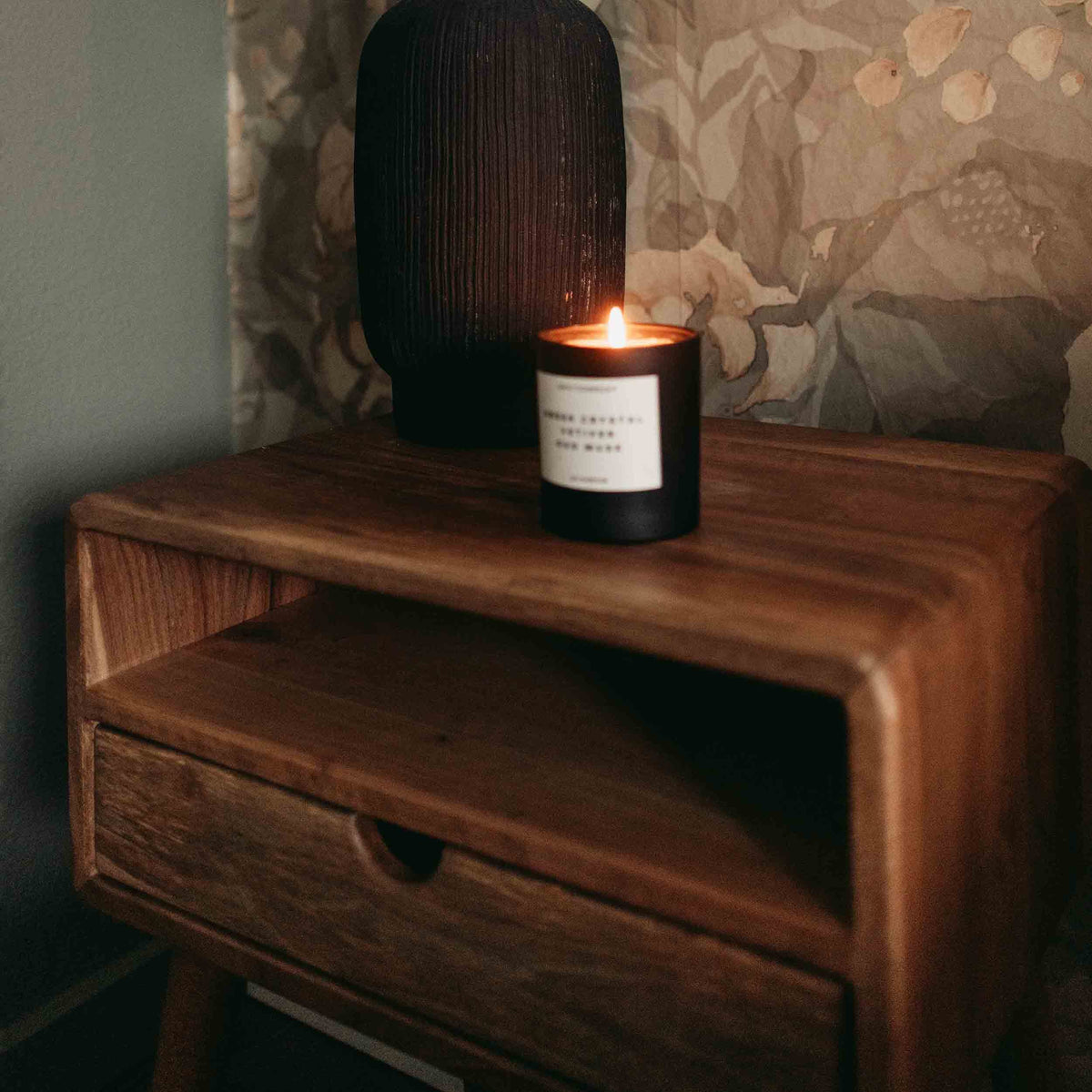 Close-up of the rounded corner, open shelf and drawer of the walnut nightstand with a candle on top