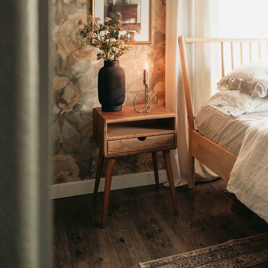 Walnut mid-century nightstand with open shelf and drawer on tapered legs beside a bed