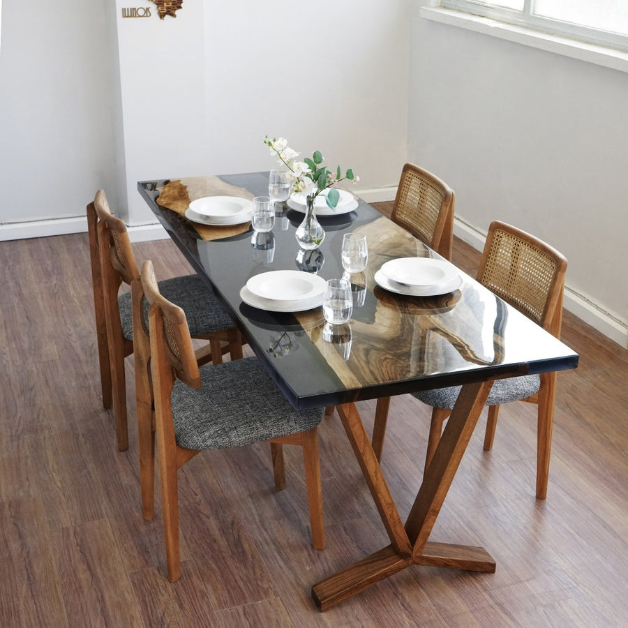 Live edge walnut dining table with a black epoxy river and wooden V legs, angled from the end with rattan back chairs
