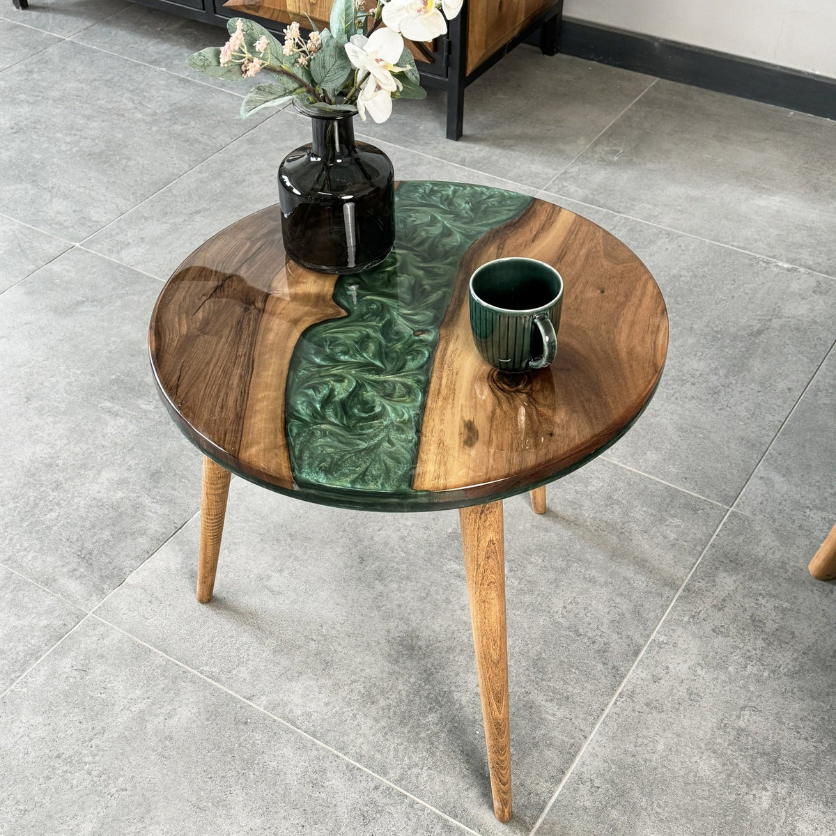 Walnut epoxy side table with a green resin river, close view from above with a dark vase and green mug