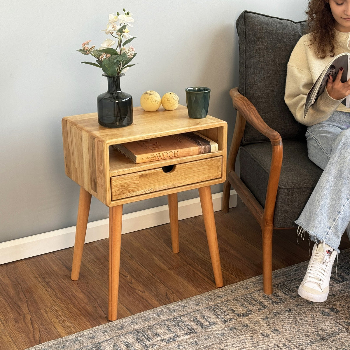 Close view of the oak nightstand top and drawer on tapered legs, with a green mug on top