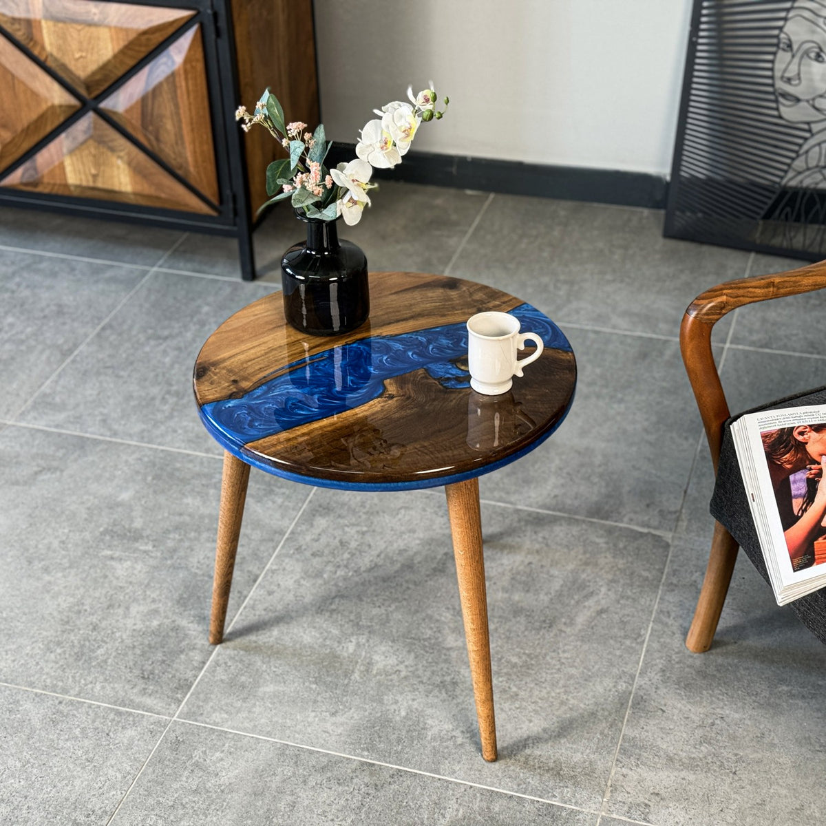 Blue epoxy river side table, closer front view with a mug and vase on the round walnut top