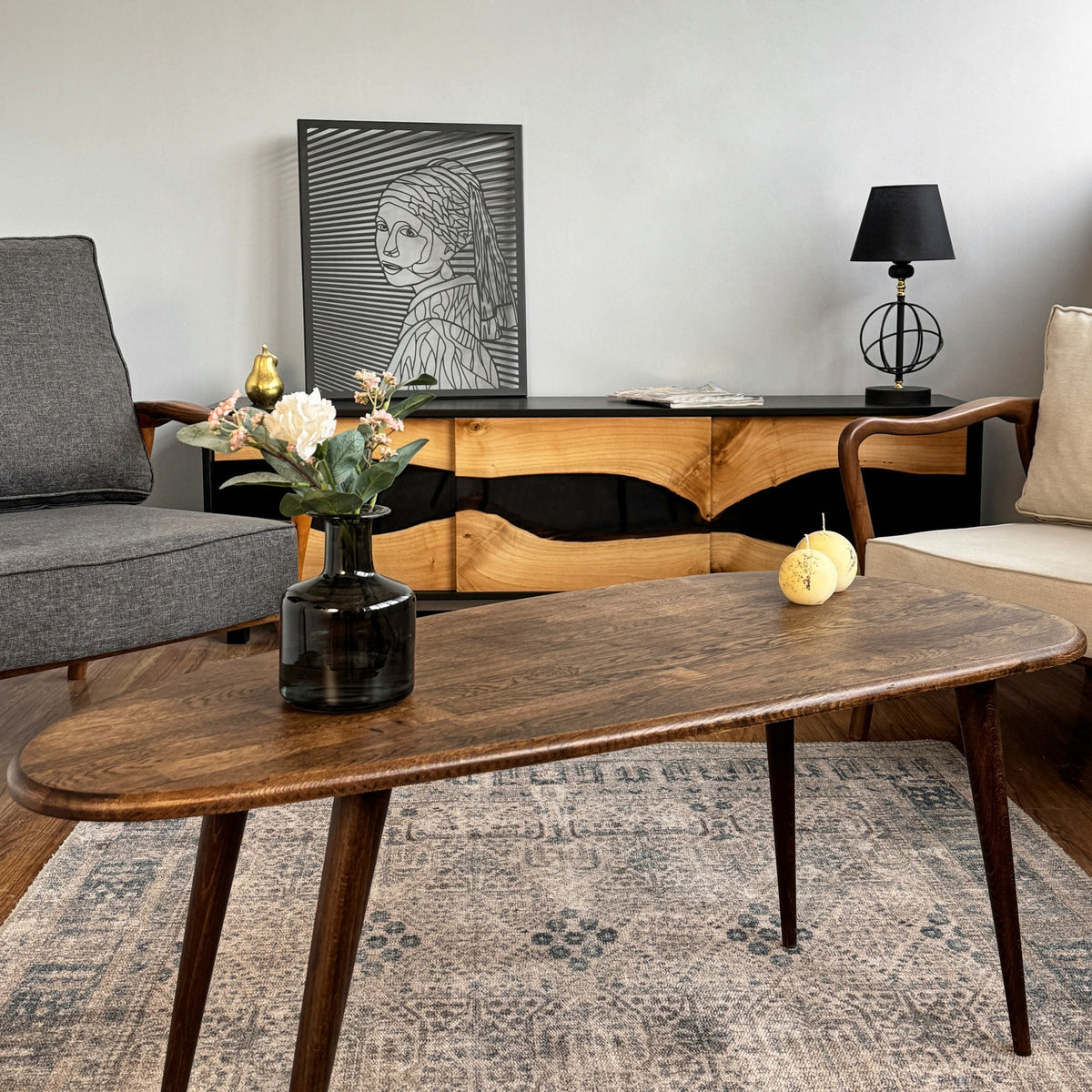 Solid oak mid century coffee table seen from the long side, with a gray armchair and console behind