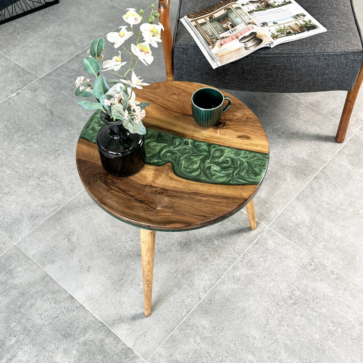 Round walnut epoxy side table with a green resin river and tapered legs, angled top view with a ceramic mug on top