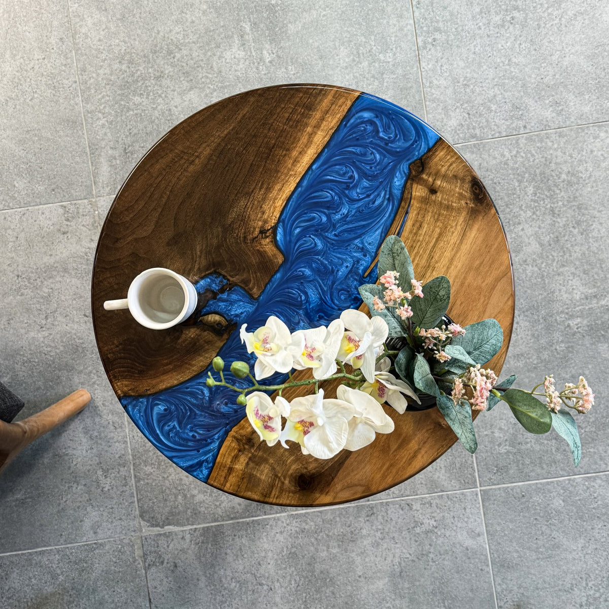 Top view of the round walnut side table with a blue epoxy river and white orchids