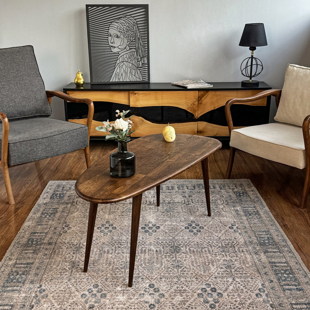 Wide view of the solid oak oval coffee table on a patterned rug between two armchairs