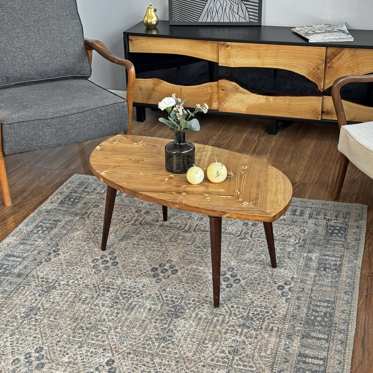 Leaf shaped solid wood coffee table with dark tapered legs in front of a gray armchair and sideboard