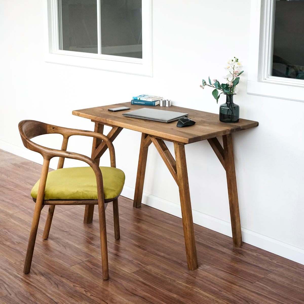 Wide view of the small walnut desk with a straight front edge, green chair and window behind