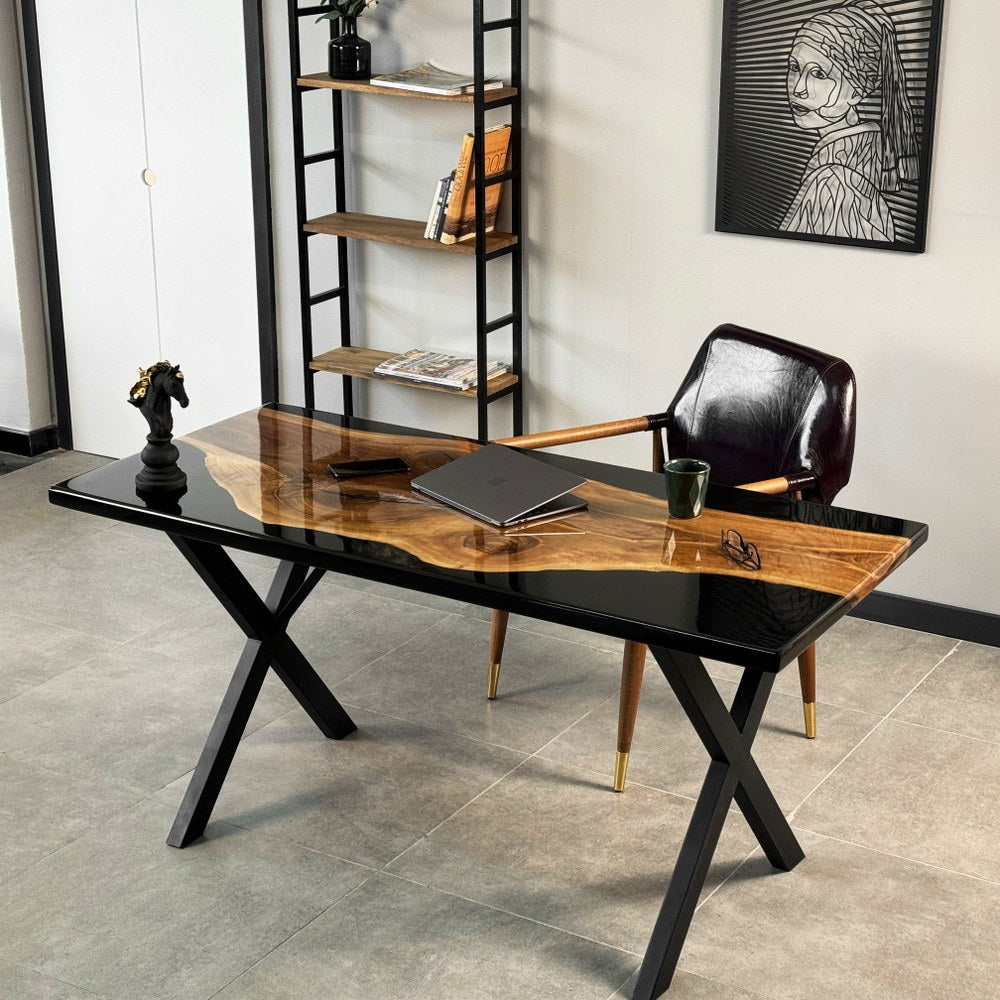 Walnut and black epoxy desk seen at an angle, black metal X legs beside a leather chair