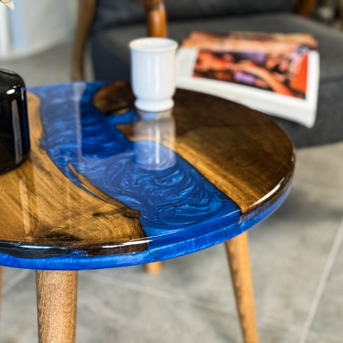 Close-up of the blue resin river and glossy walnut edge on the round table with a mug and magazine
