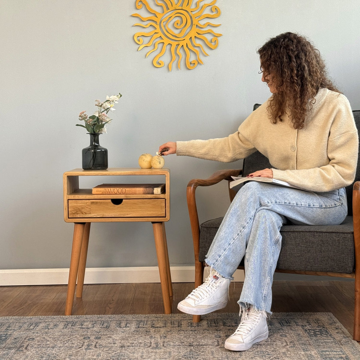 Oak nightstand with a seated woman reaching toward the top, drawer and open cubby visible