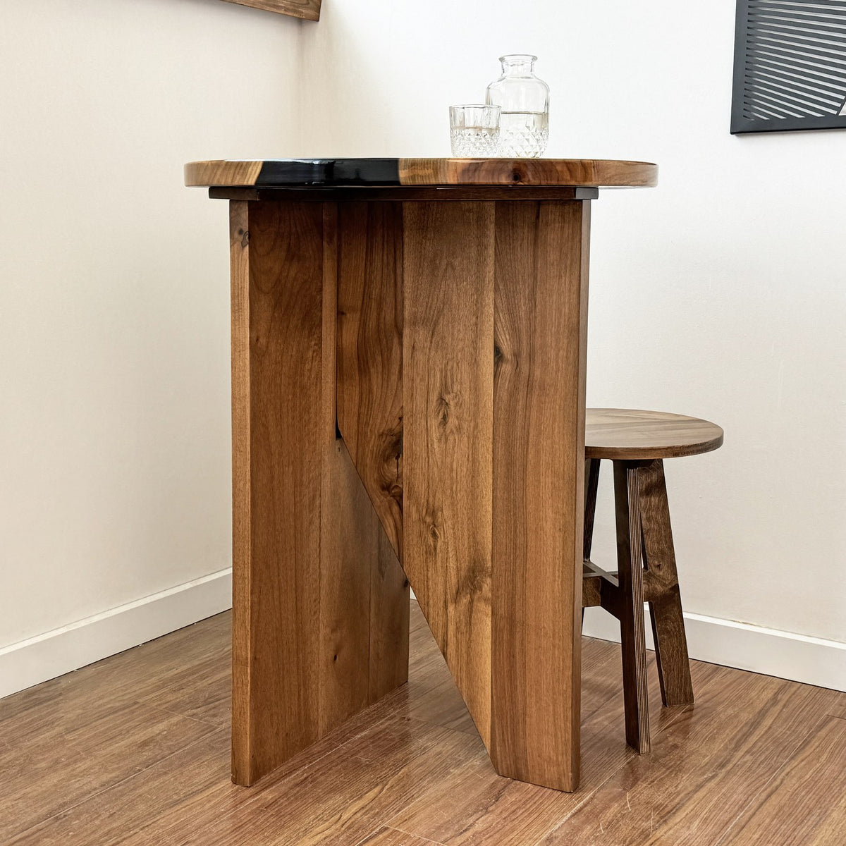 Walnut round bar table with a black epoxy river and a stool at its side, viewed from the left