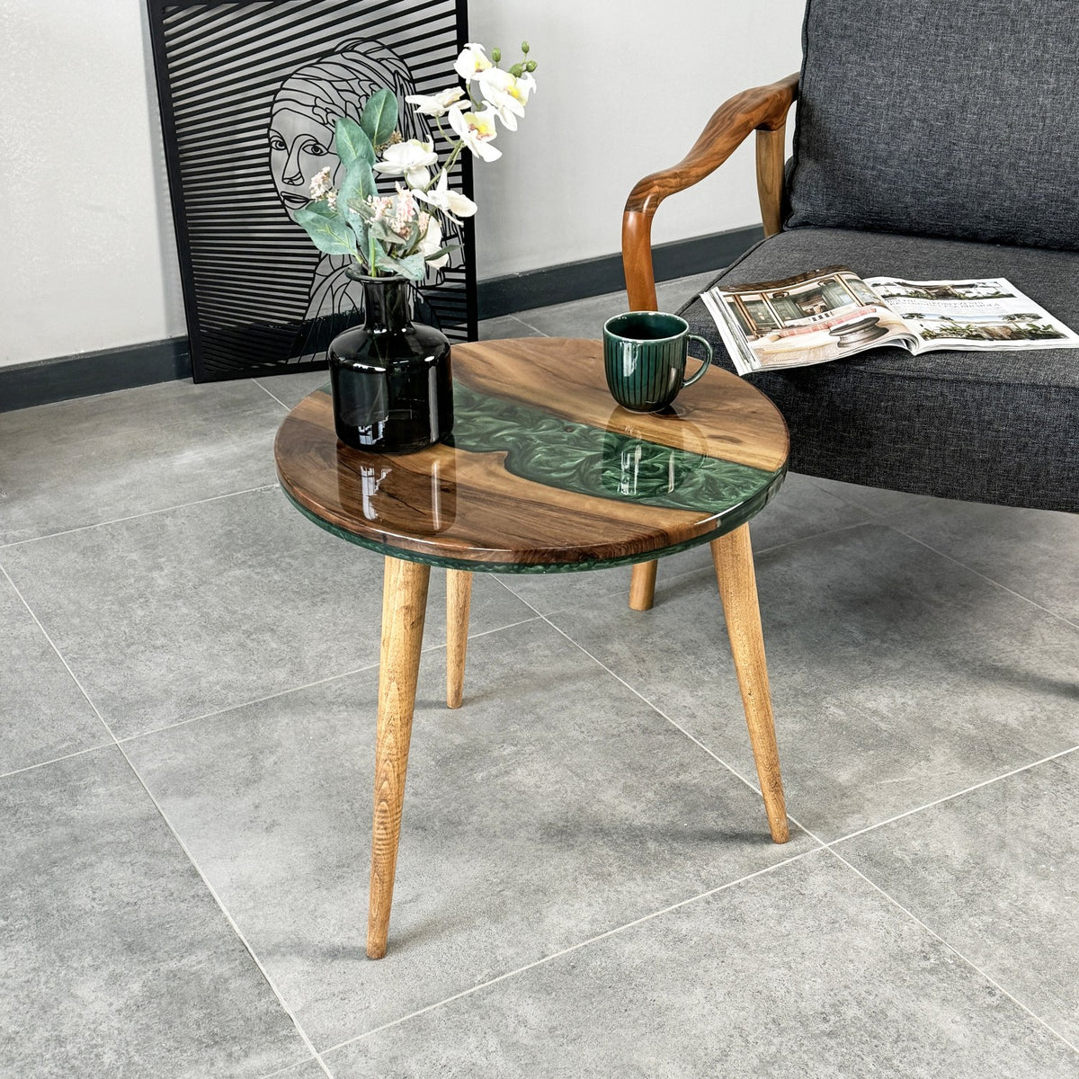 Round walnut epoxy side table with green resin beside an armchair, seen from a low angle