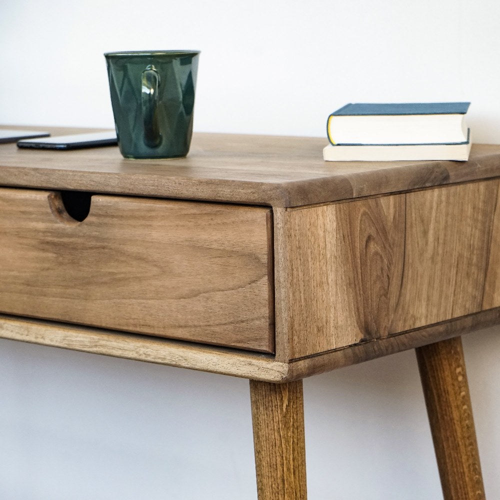 Close-up of the walnut desk's drawer front with finger notch, grain and a tapered leg