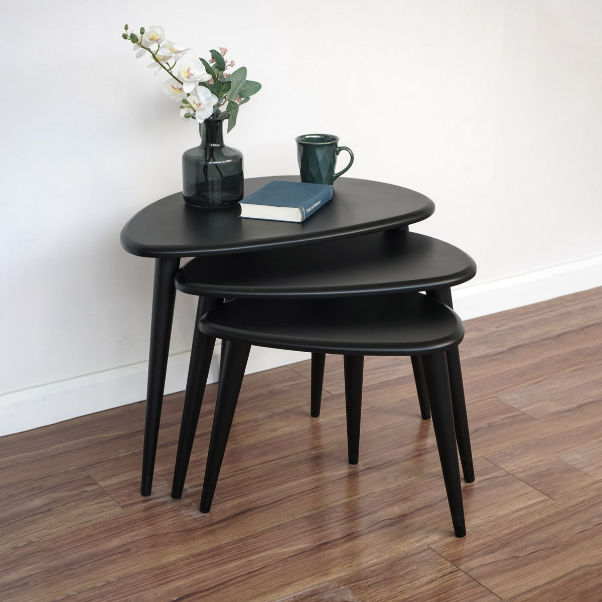 Set of three matte black Ercol Pebble style nesting tables with tapered legs in a room corner