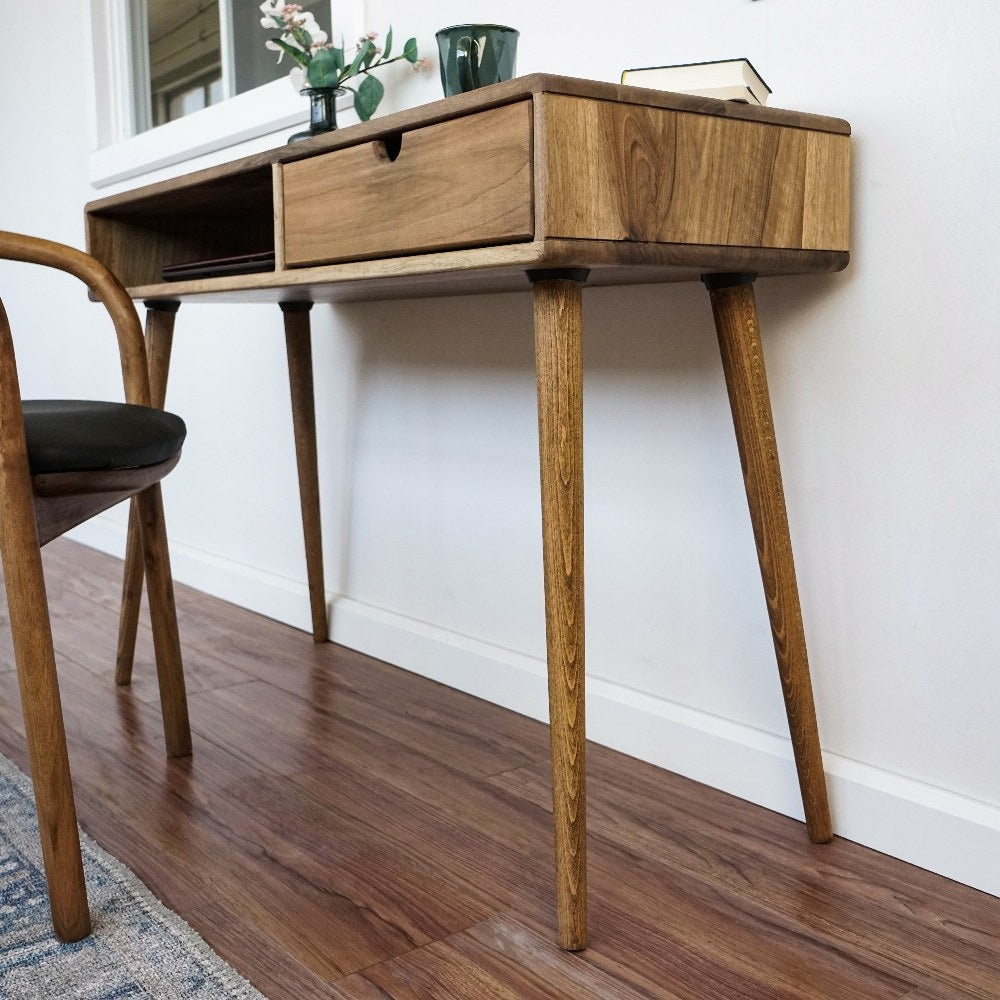 Low side view of the walnut desk's tapered legs and drawer from the right
