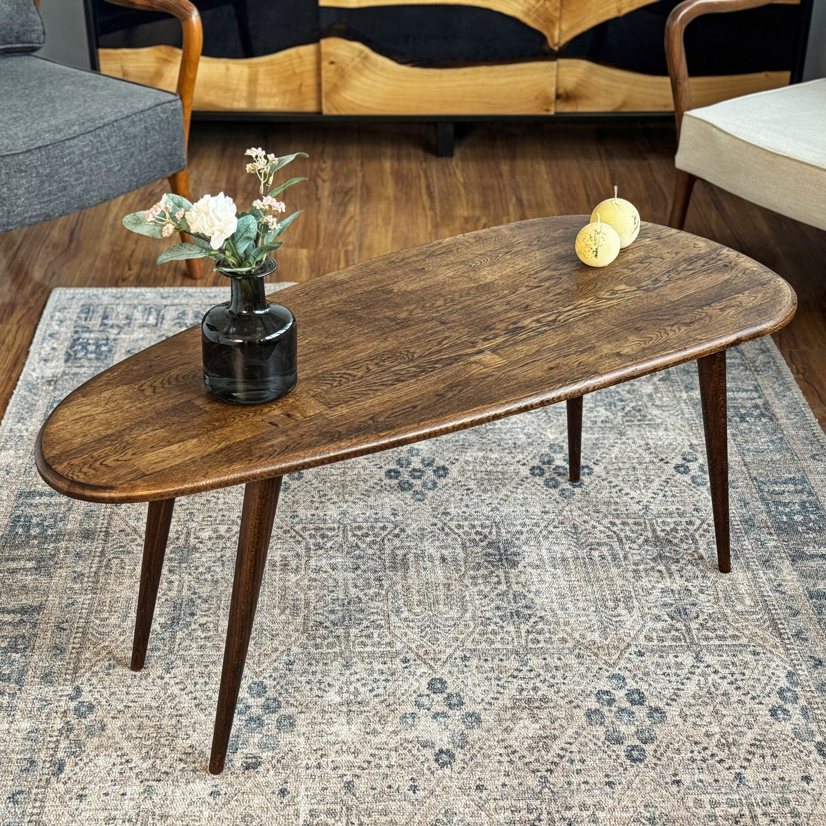 Angled view of the oak oval coffee table, narrow end toward the camera and a vase on the top