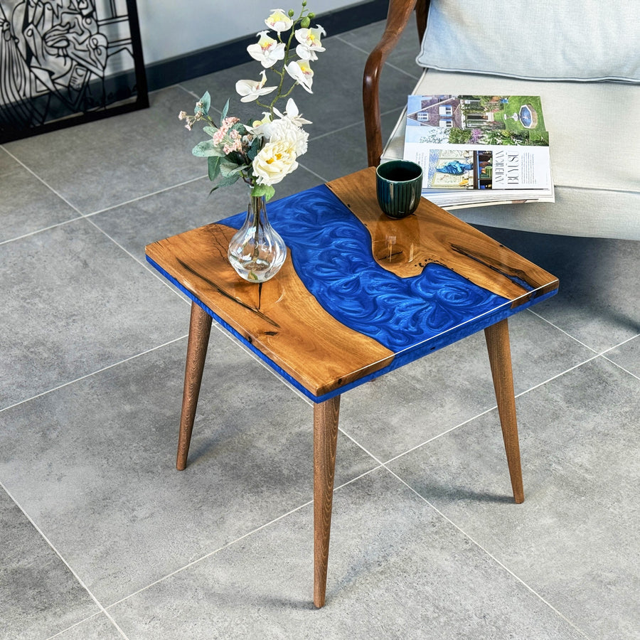 Square walnut side table with a blue epoxy river and tapered legs, angled view with a glass vase on top