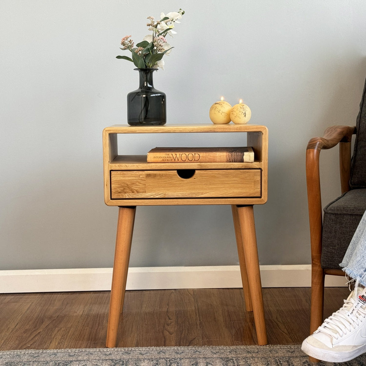 Light oak nightstand with open cubby, drawer and round finger cutout against a light blue wall