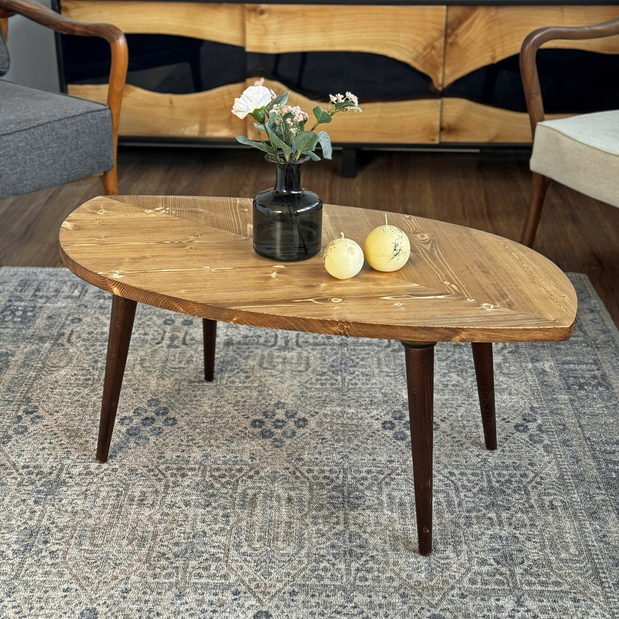 Leaf shaped solid wood coffee table with a dark walnut-tone top and tapered legs on a patterned rug