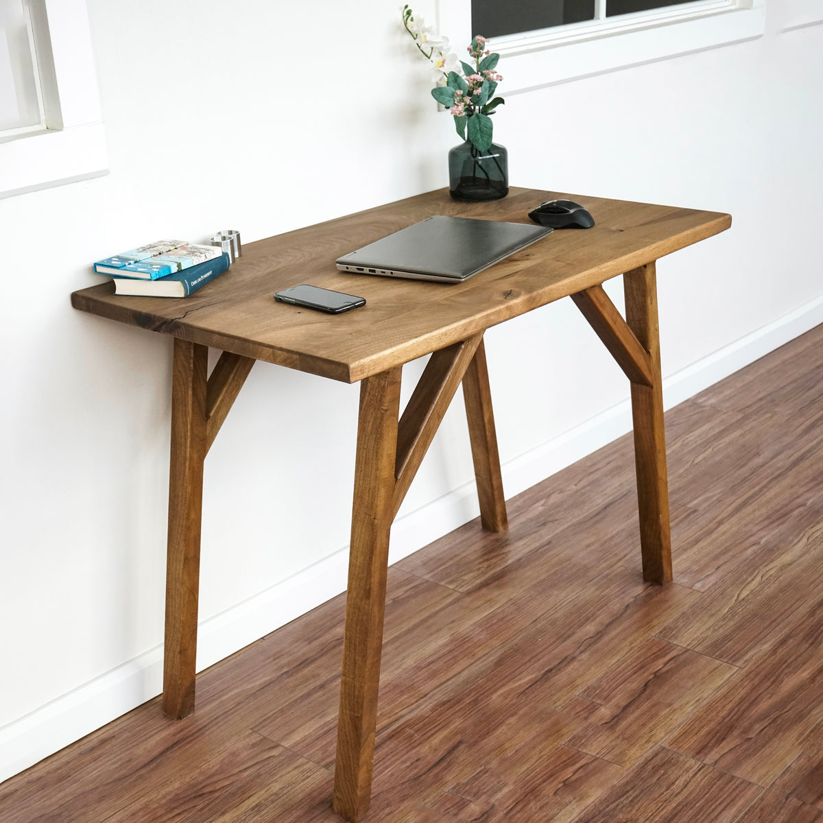 Straight-edge small walnut desk with braced wooden legs, viewed from the front left